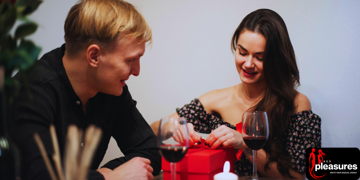 A couple at a dinner table with wine and red Valentine's gifts between them.
