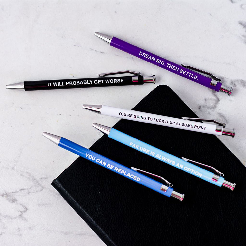 Five pens with demotivational quotes on a white surface.