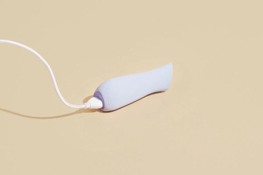 A lavender ergonomic vibrator with a white charging cable.