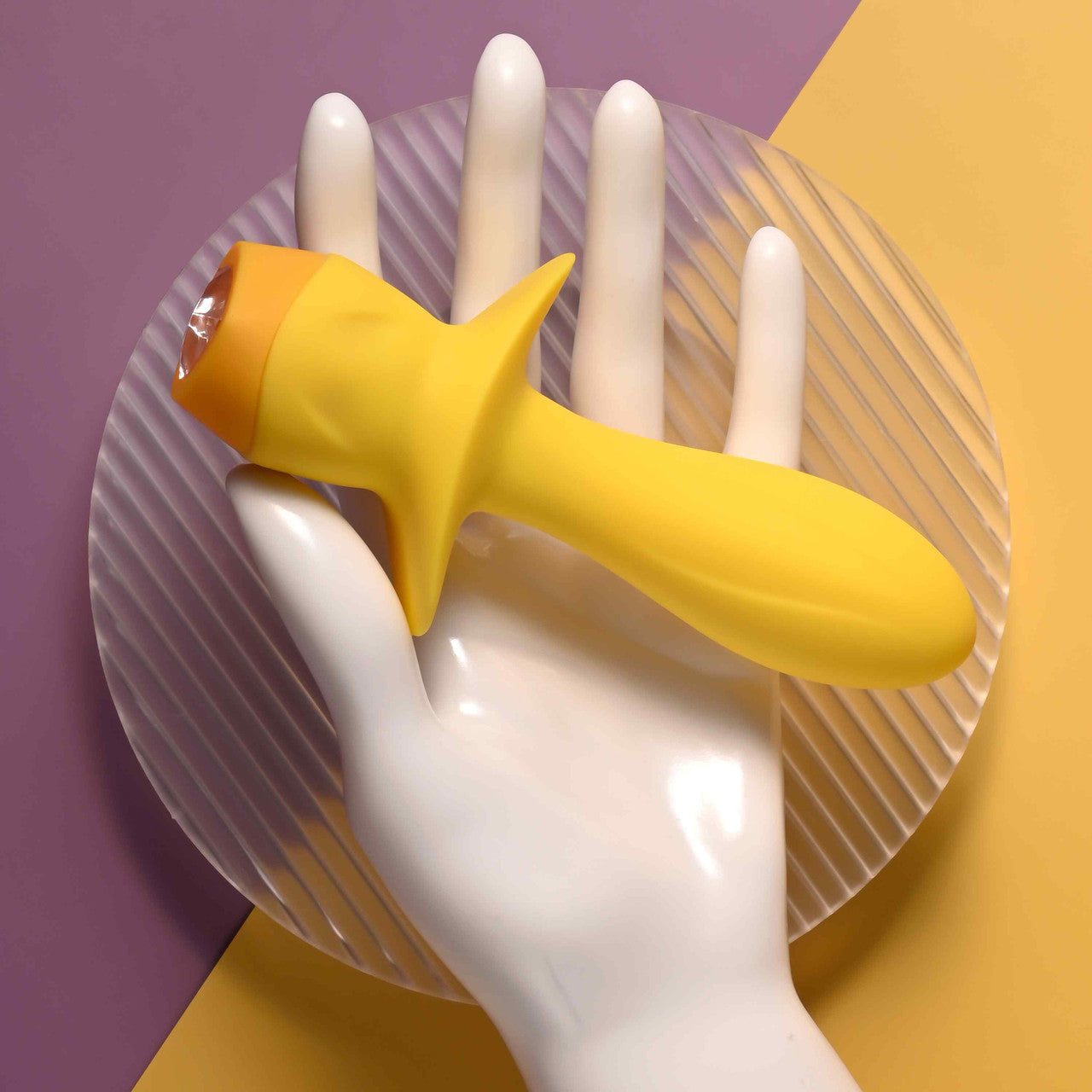 Yellow silicone vibrating plug with a clear gem on a white mannequin hand.