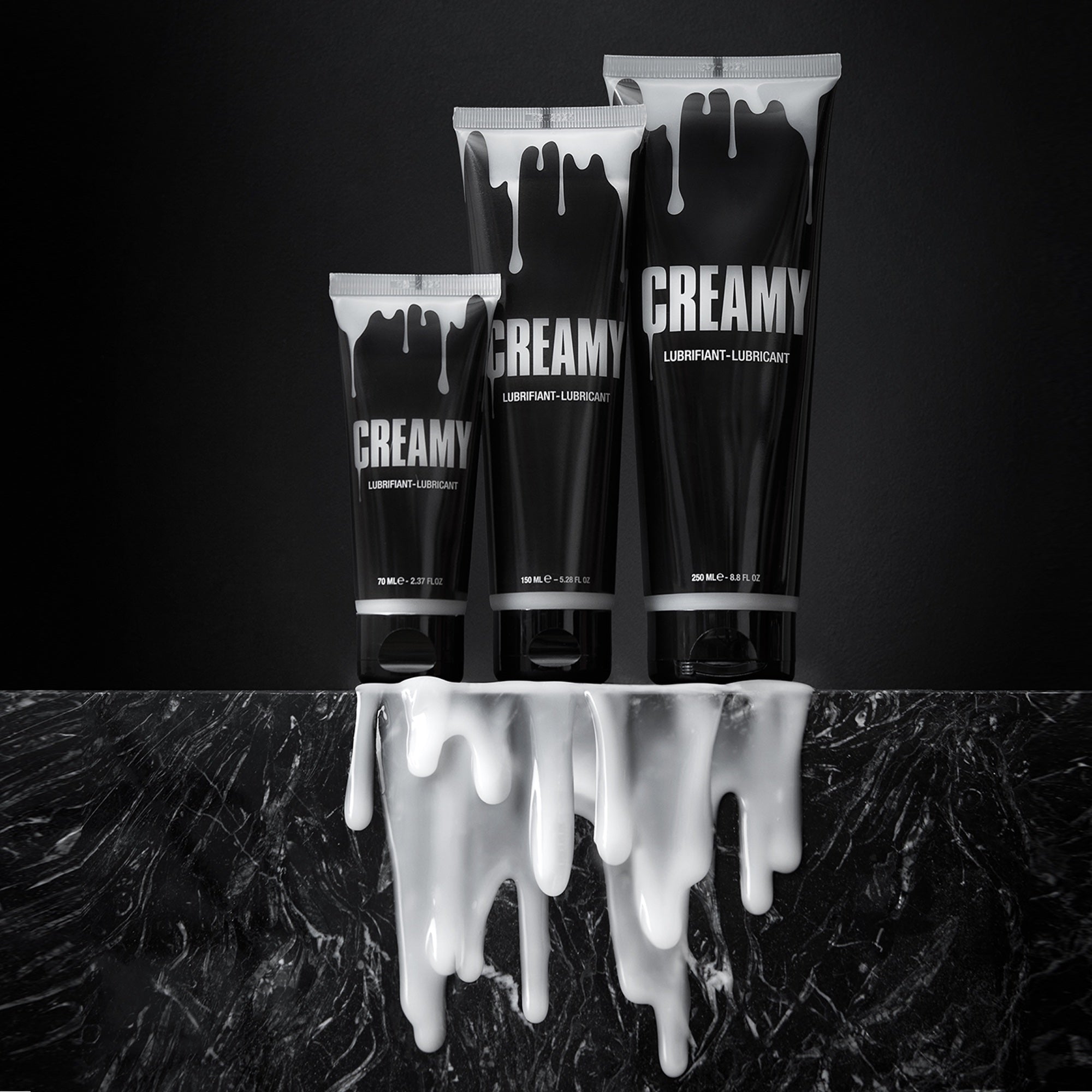 Three black tubes of "Creamy" lubricant with white drips on a dark marble surface.
