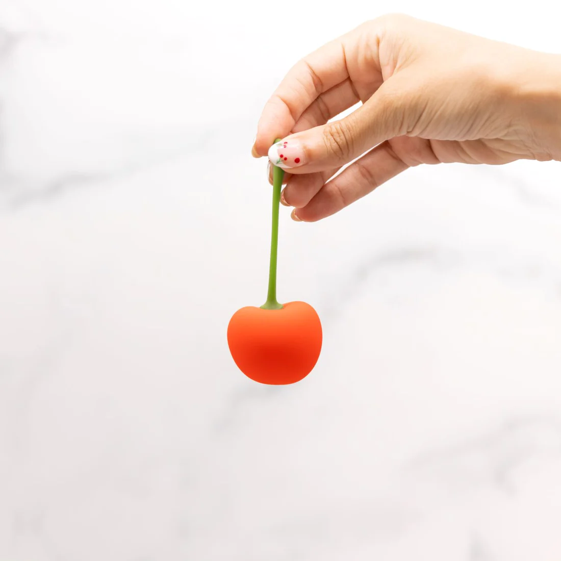 A hand holds a red cherry-shaped vibrator with a green stem.