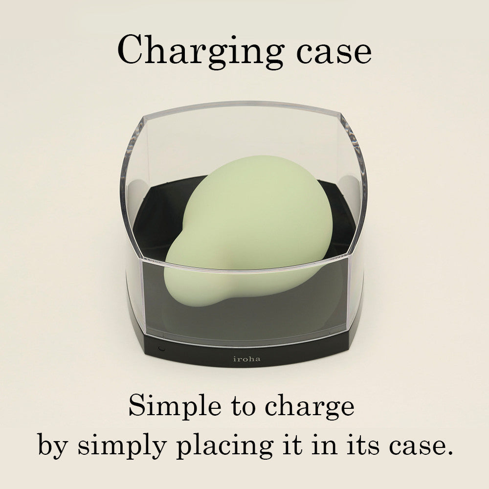 A light green silicone vibrator sits in its black and clear charging case.