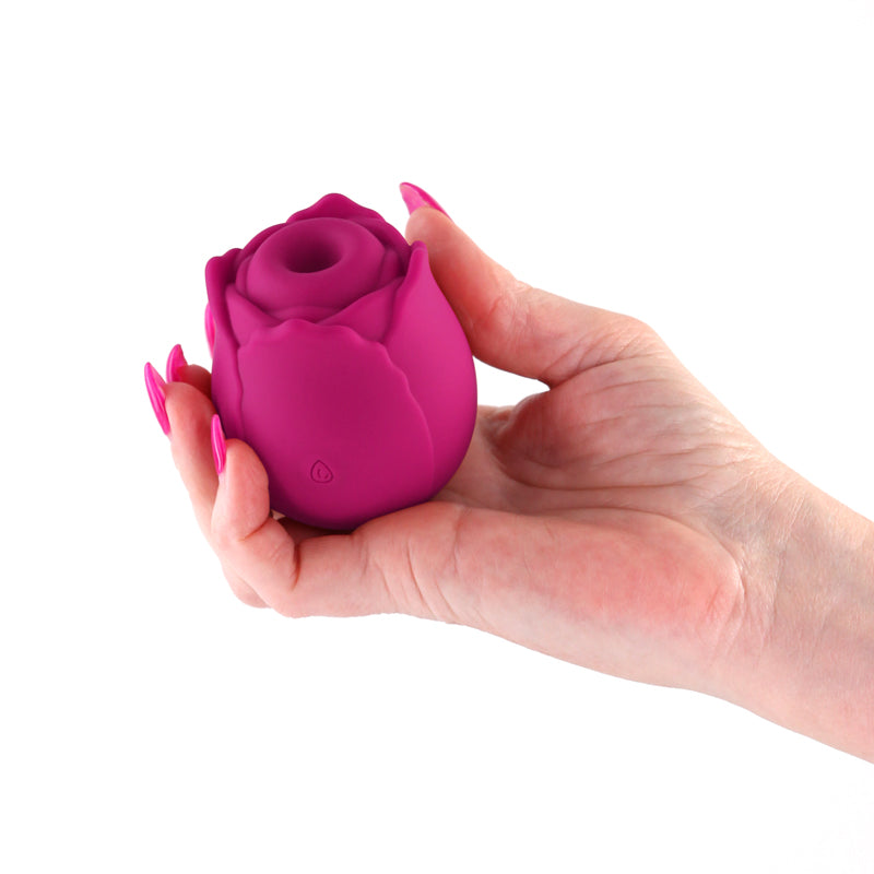 A hand holds a pink rose-shaped silicone massager with a textured opening.