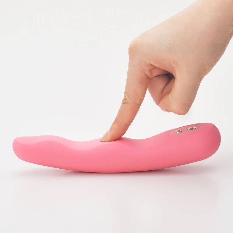 A pink flexible silicone vibrator with a finger pressing on it.