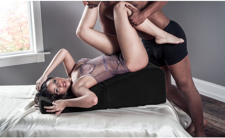 Black microvelvet flip ramp sex positioning pillow on a bed.