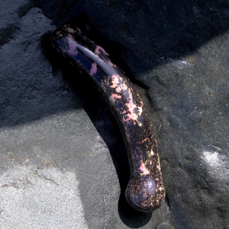 Curved rhodonite crystal wand with pink and black patterns.
