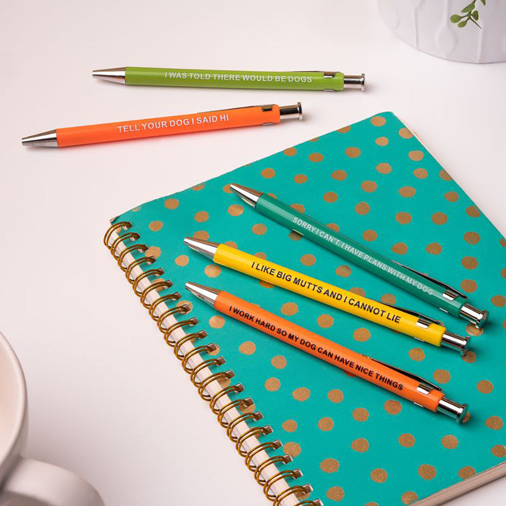 Five colorful pens with dog-themed sayings on a polka dot notebook.