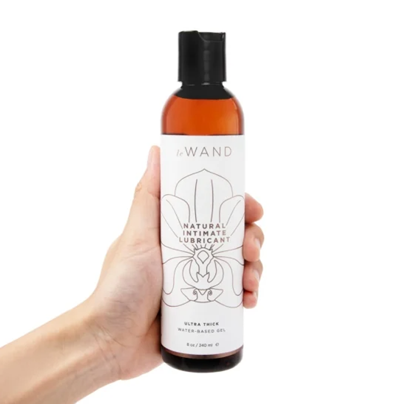 A hand holds a bottle of Le Wand Natural Intimate Lubricant.