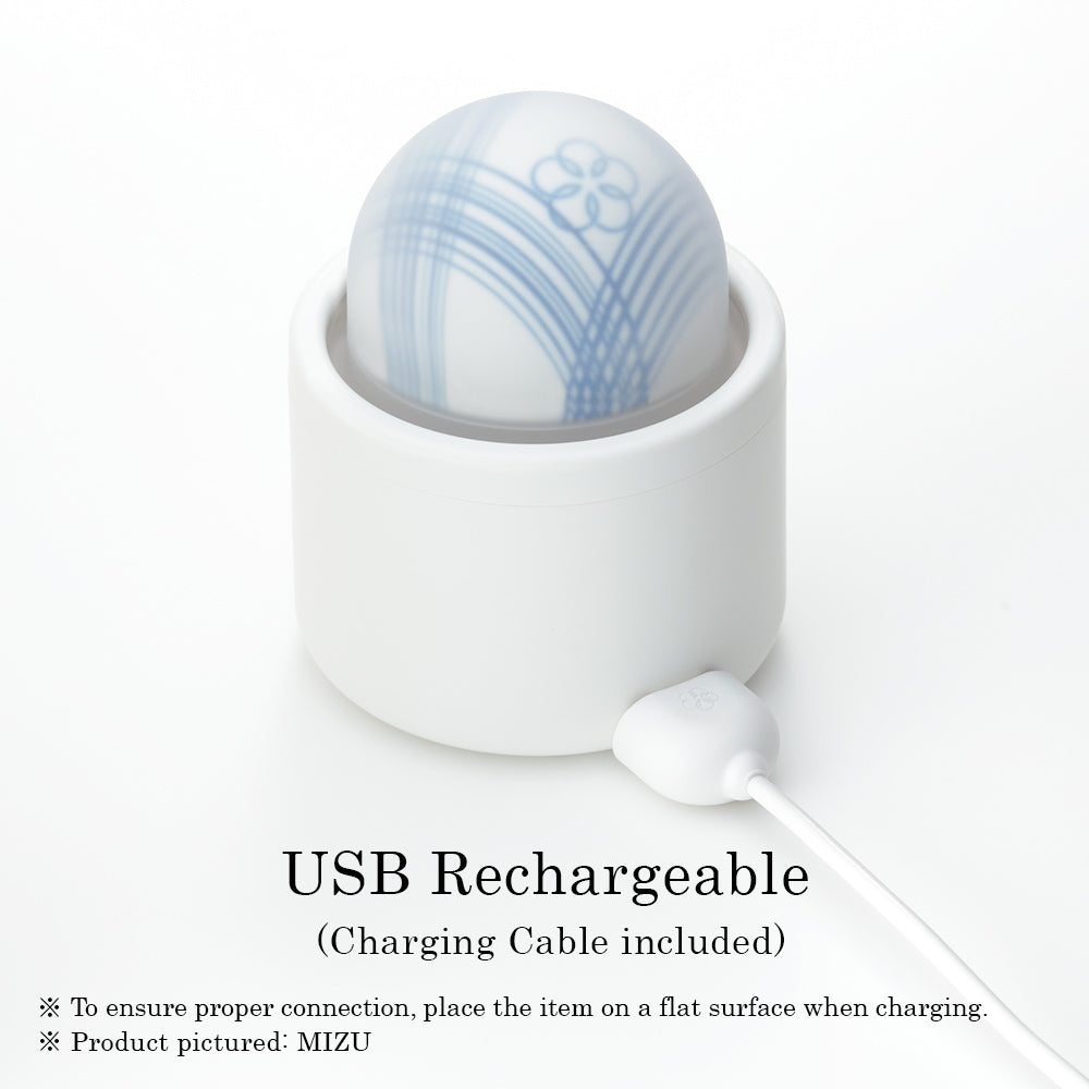A white cylindrical base holds a translucent, dome-shaped massager with blue floral patterns, connected to a white USB charging cable.
