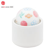A white cylindrical base holds a round, patterned massager with floral designs.