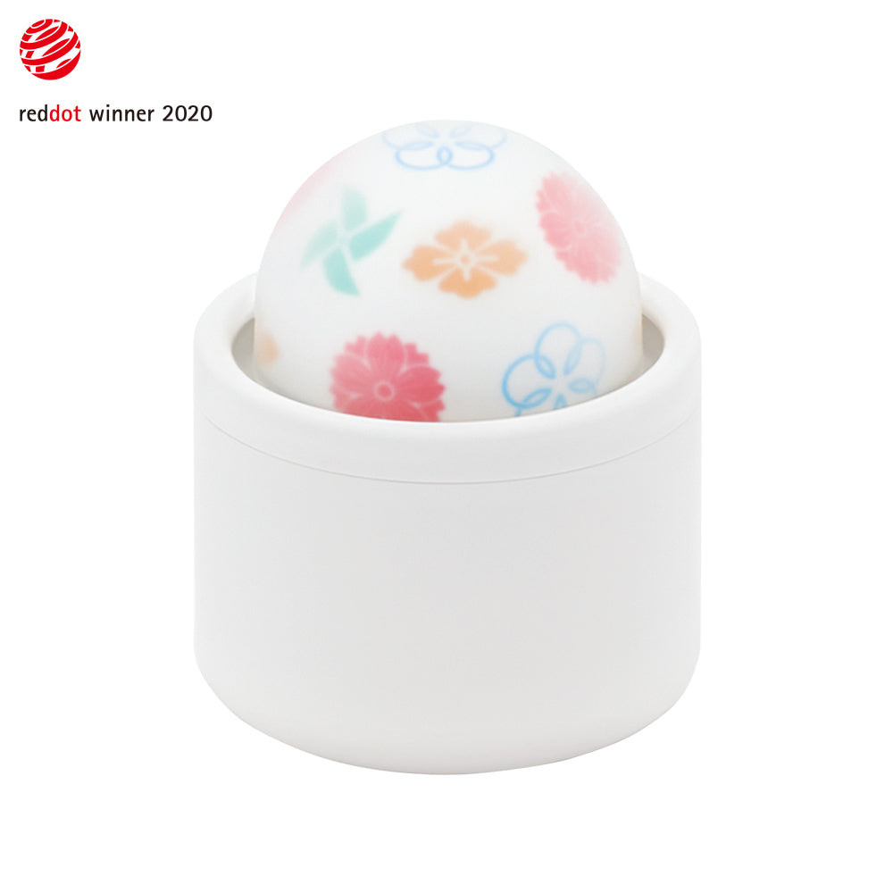 A white cylindrical base holds a round, patterned massager with floral designs.
