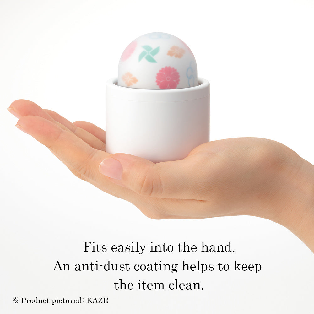 A hand holds a white cylindrical case with a patterned egg-shaped massager inside.