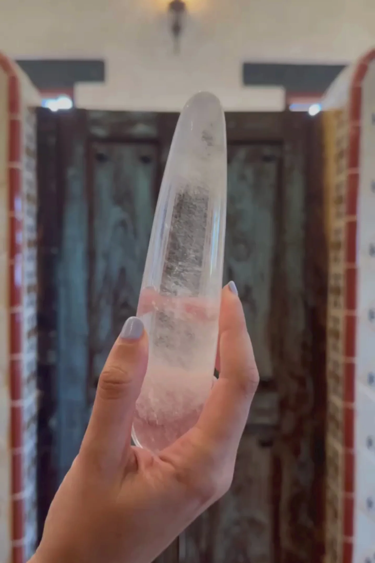 Clear quartz crystal wand with a tapered end held in a hand.