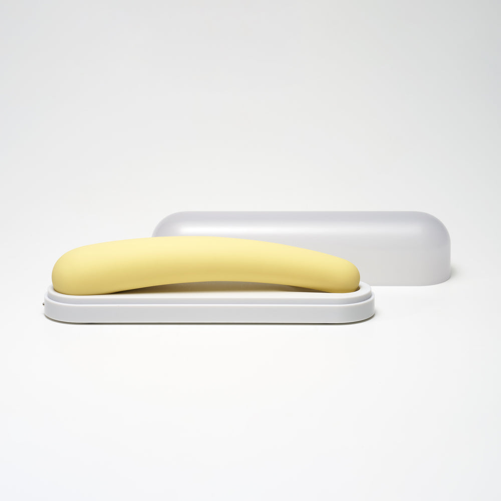 Yellow silicone vibrator with a crescent shape on a white base with a grey cover.