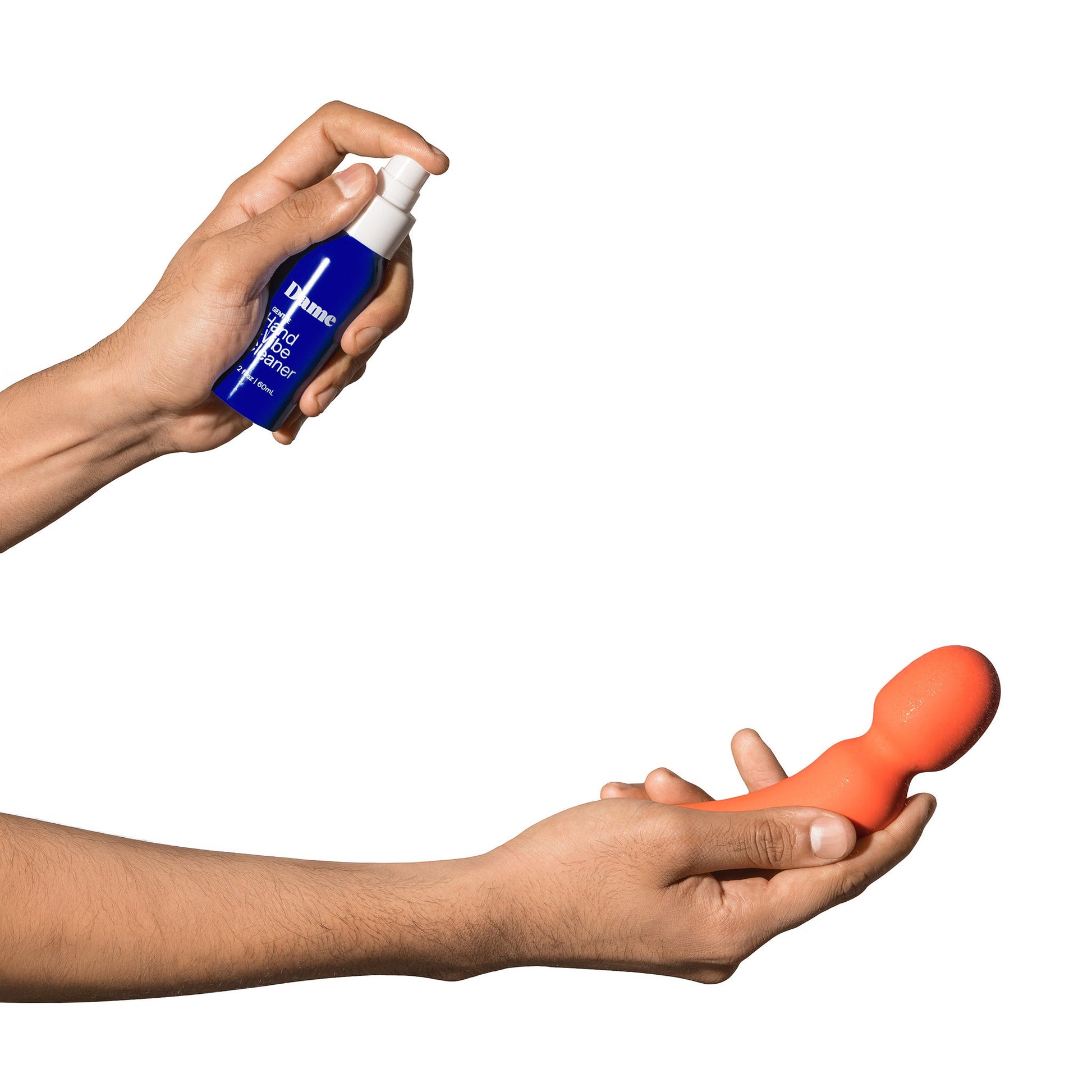 A hand holds a blue spray bottle of Dame Hand and Vibe Cleaner, while another hand holds an orange vibrator.