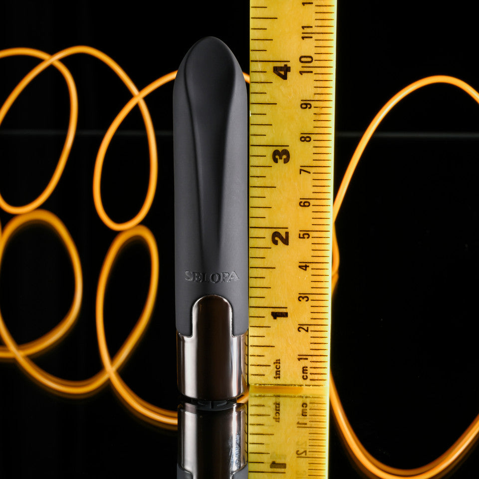A black silicone bullet vibrator with a silver base is shown next to a ruler.