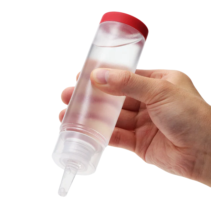 A hand holds a clear squeeze bottle with a red cap, containing a mild water-based lubricant.