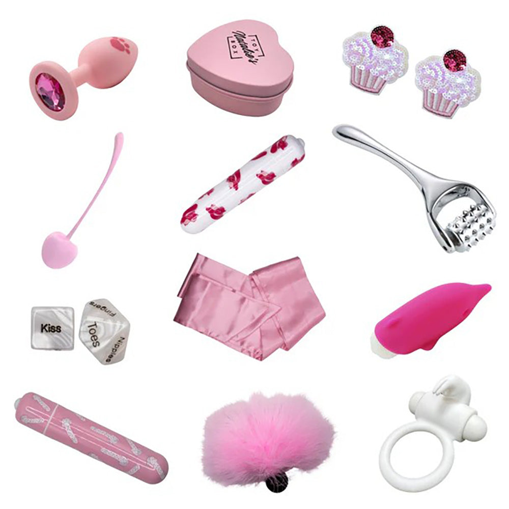 A pink heart-shaped box with a toy inside, a pink butt plug, a pink wand, a pink fluffy item, a pink vibrator, a pink ring, a pink satin scarf, a pink and white patterned toy, a metal massager, and two cupcake-shaped items.