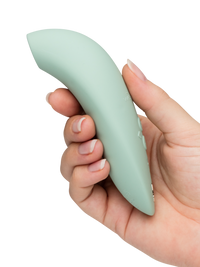 A hand holds a sage green We-Vibe Melt 2 clitoral stimulator.