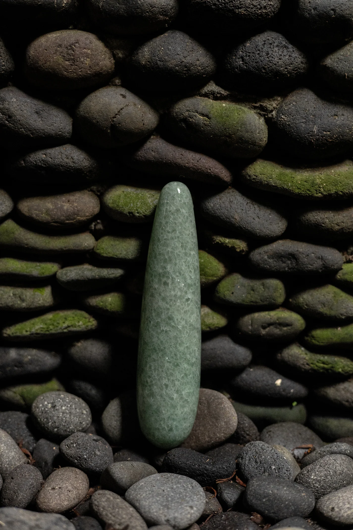 Green aventurine crystal wand on a bed of stones.