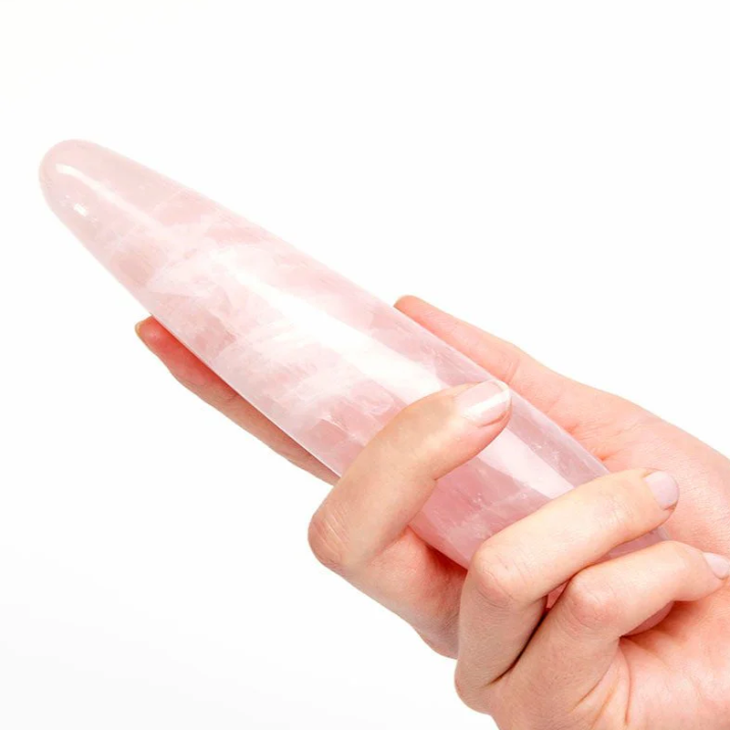 A hand holds a smooth, pink rose quartz crystal wand.