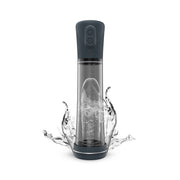 A dark grey and clear penis pump with water splashing around its base.