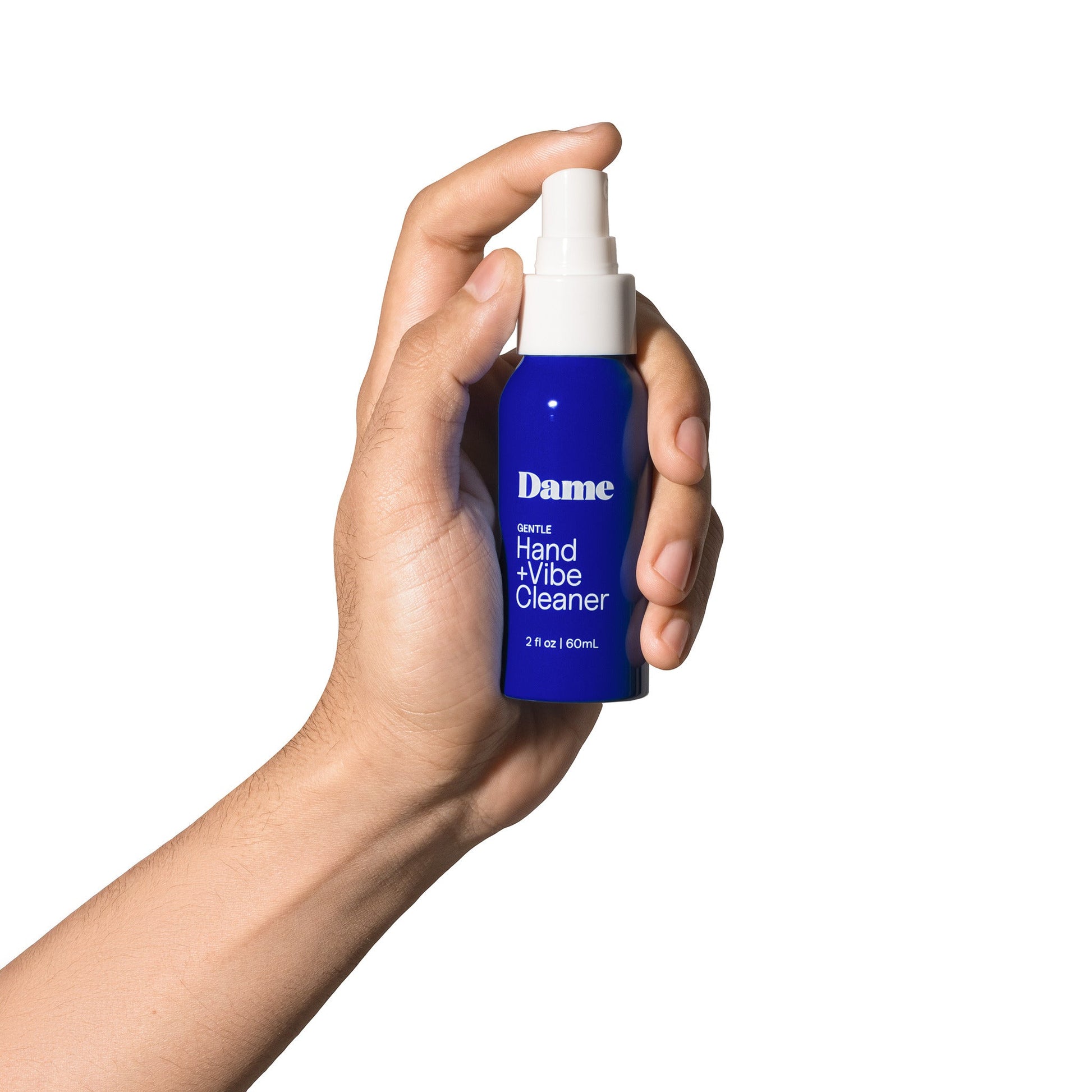 A hand holds a blue spray bottle of Dame Hand + Vibe Cleaner.