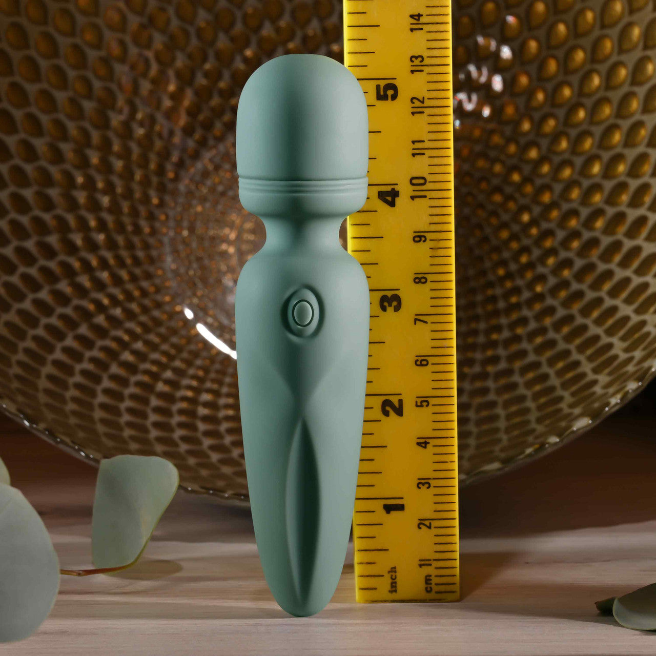 A teal silicone vibrator with a textured grip and a circular button, measured against a ruler.