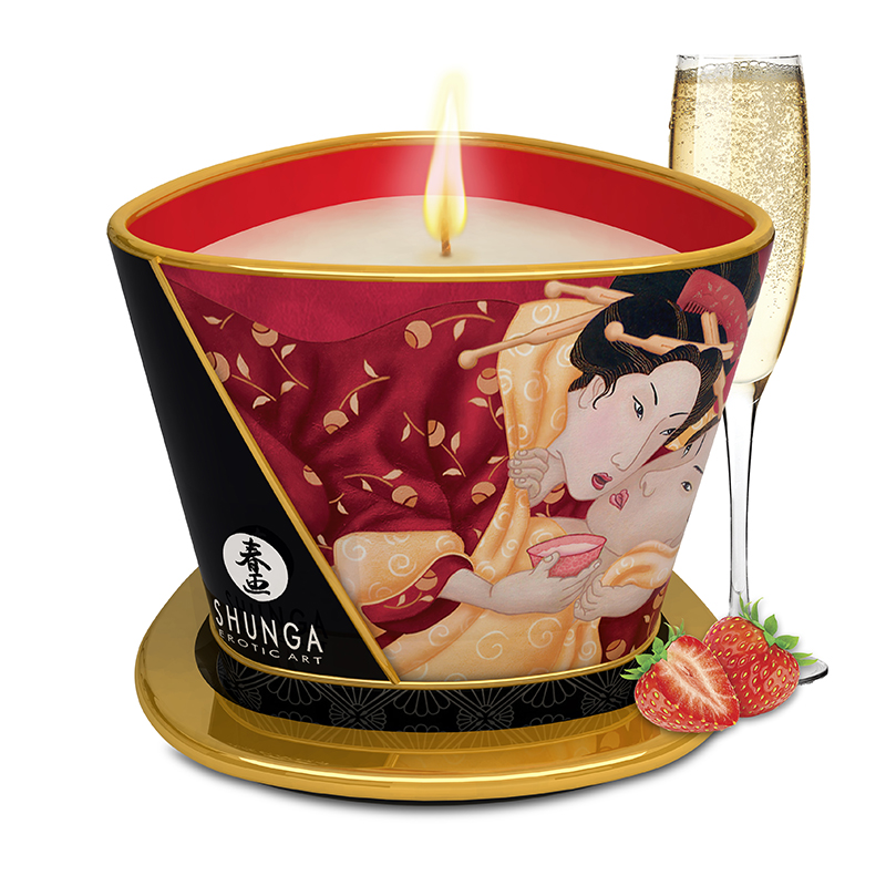 A lit soy massage candle with a strawberry scent and erotic art on the container, next to a glass of champagne and strawberries.
