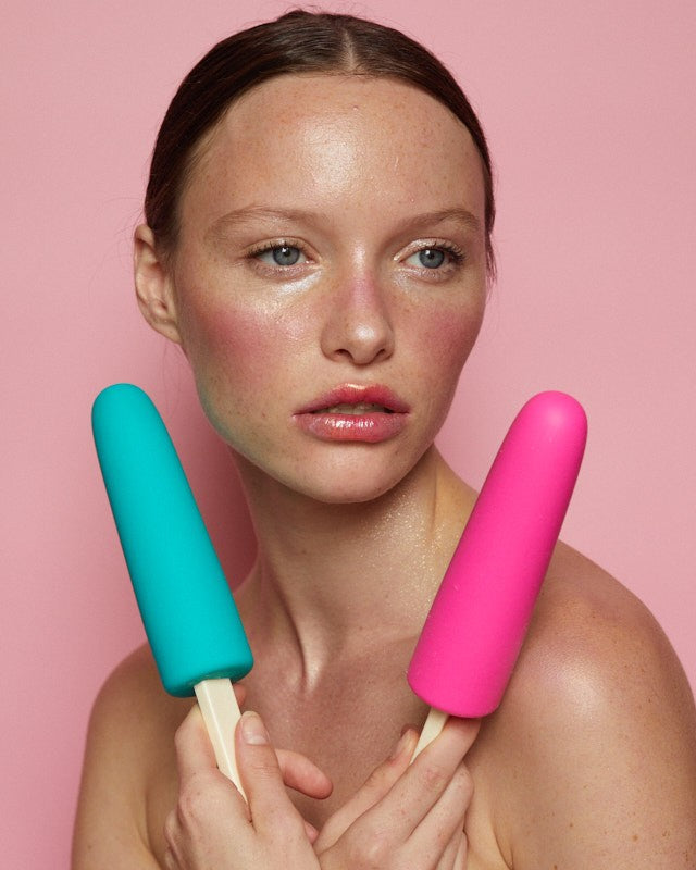 A pink silicone cooling dildo shaped like a popsicle, held by a model against a pink background.