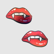 Two red vampire lips with fangs nipple pasties on a gray background.