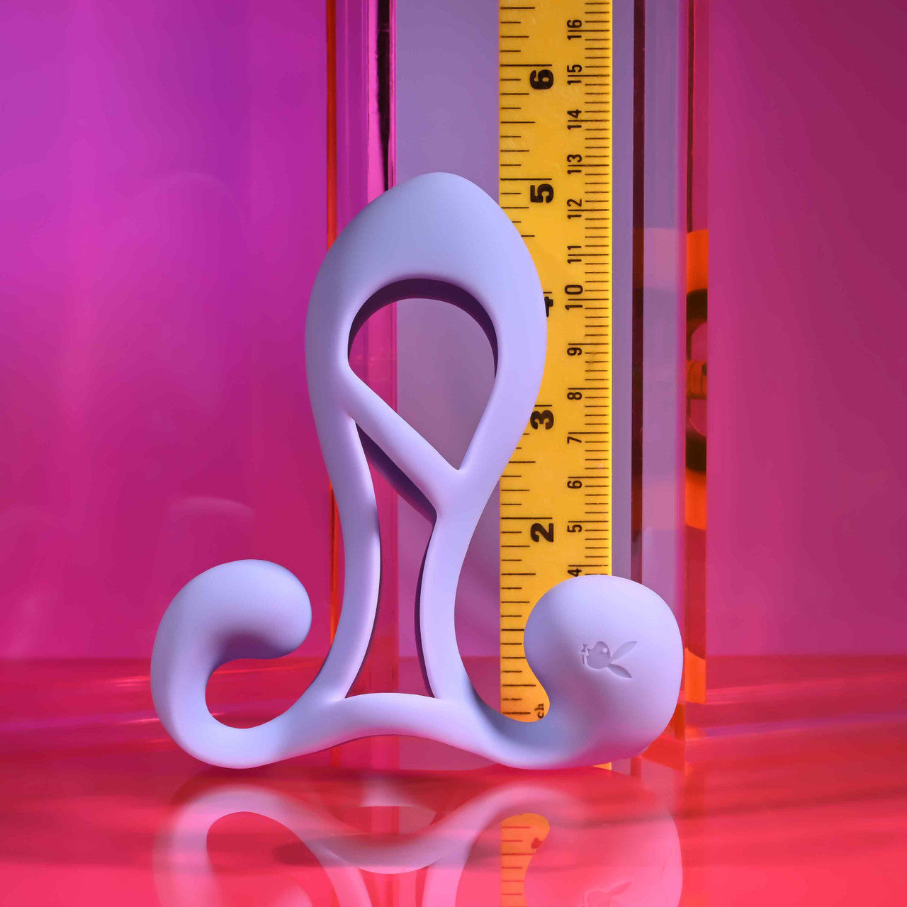 A purple silicone penis enhancer cage with a Playboy bunny logo, next to a ruler.
