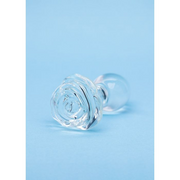 A clear glass butt plug shaped like a rose on a blue background.