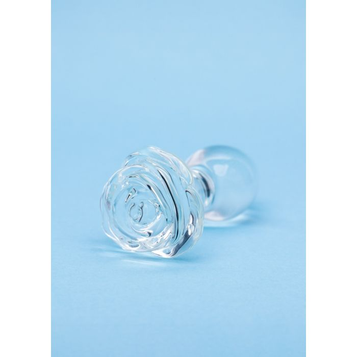A clear glass butt plug shaped like a rose on a blue background.