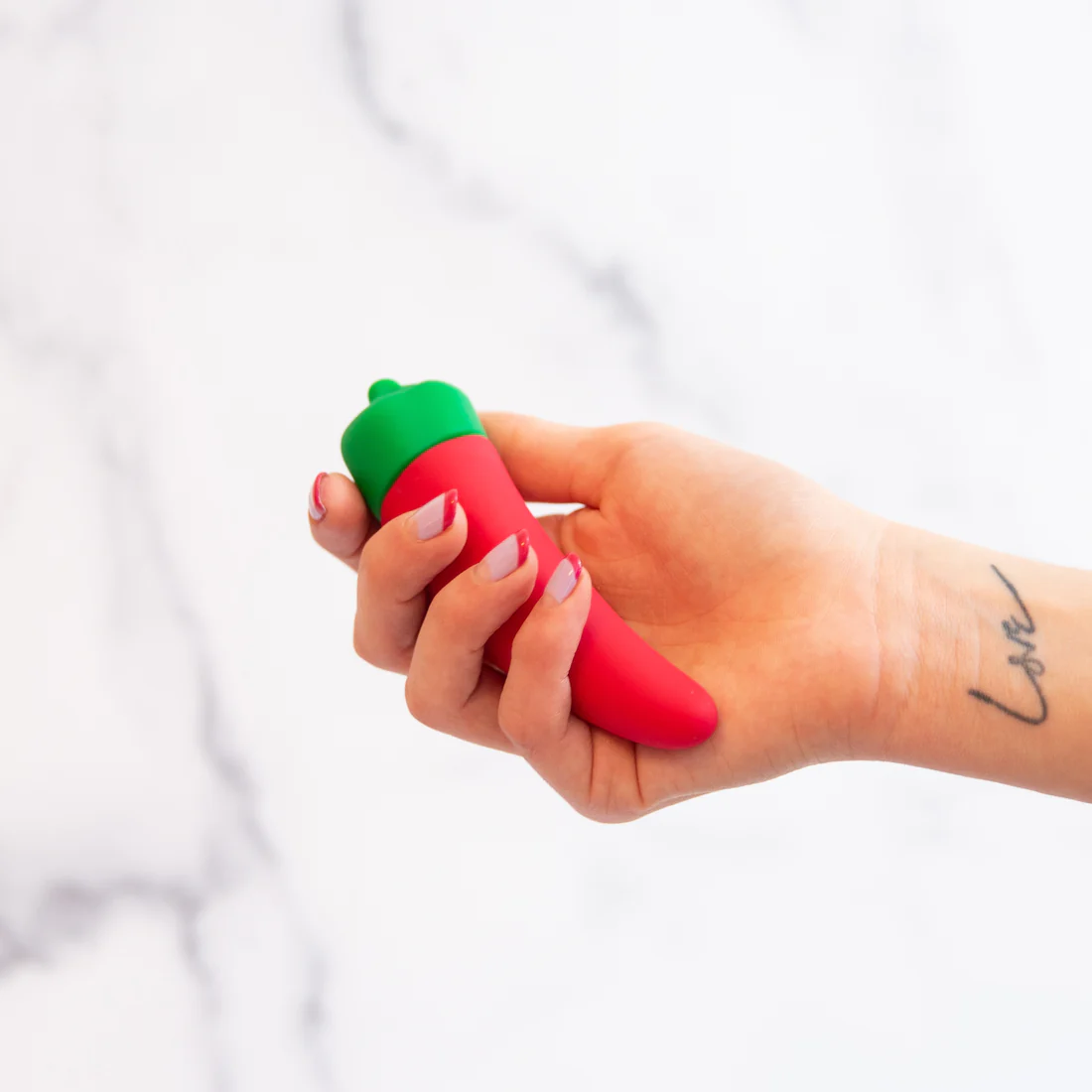 A hand holds a red and green chili pepper shaped silicone vibrator.