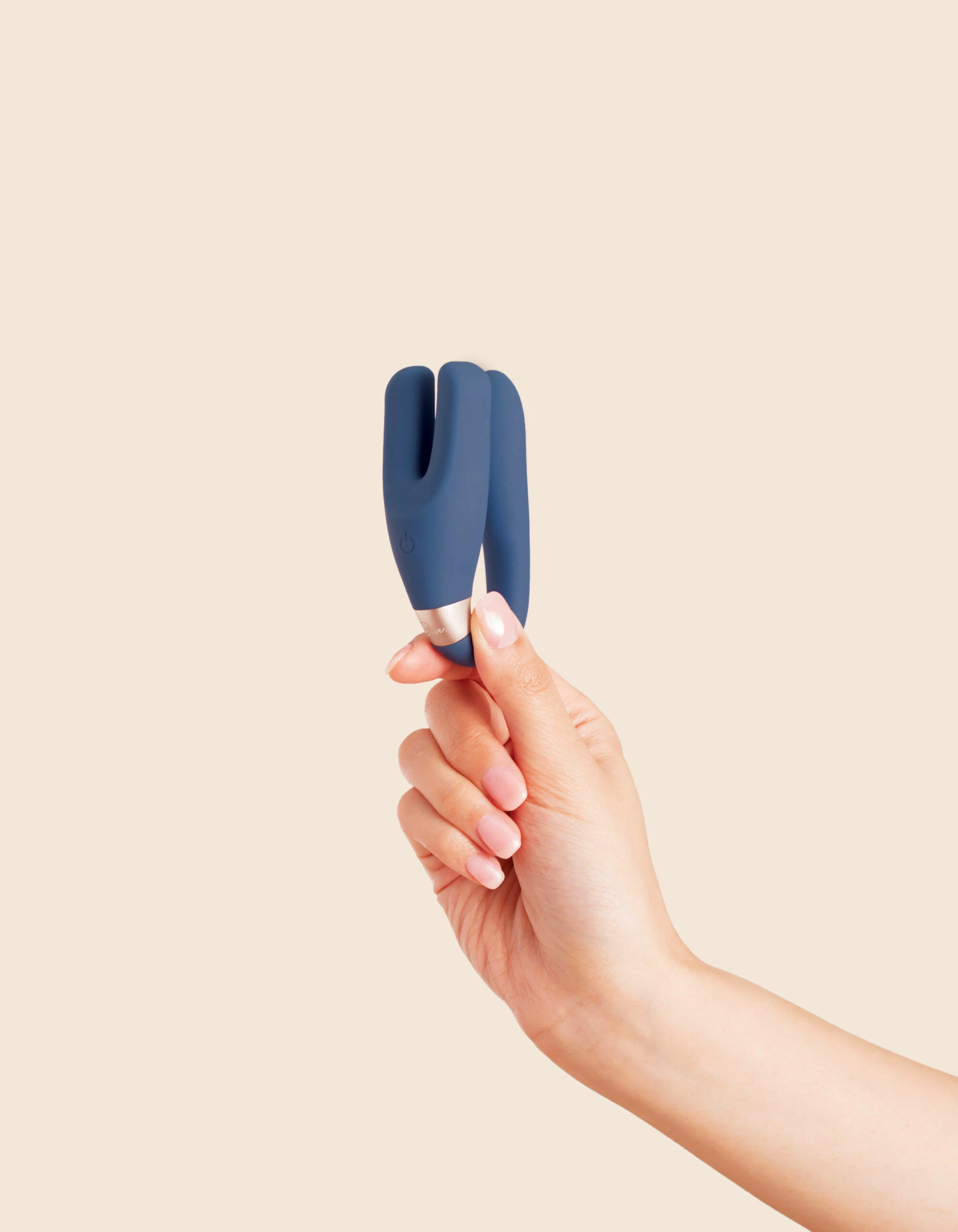 A hand holds a blue wearable remote control vibrator with a gold band.