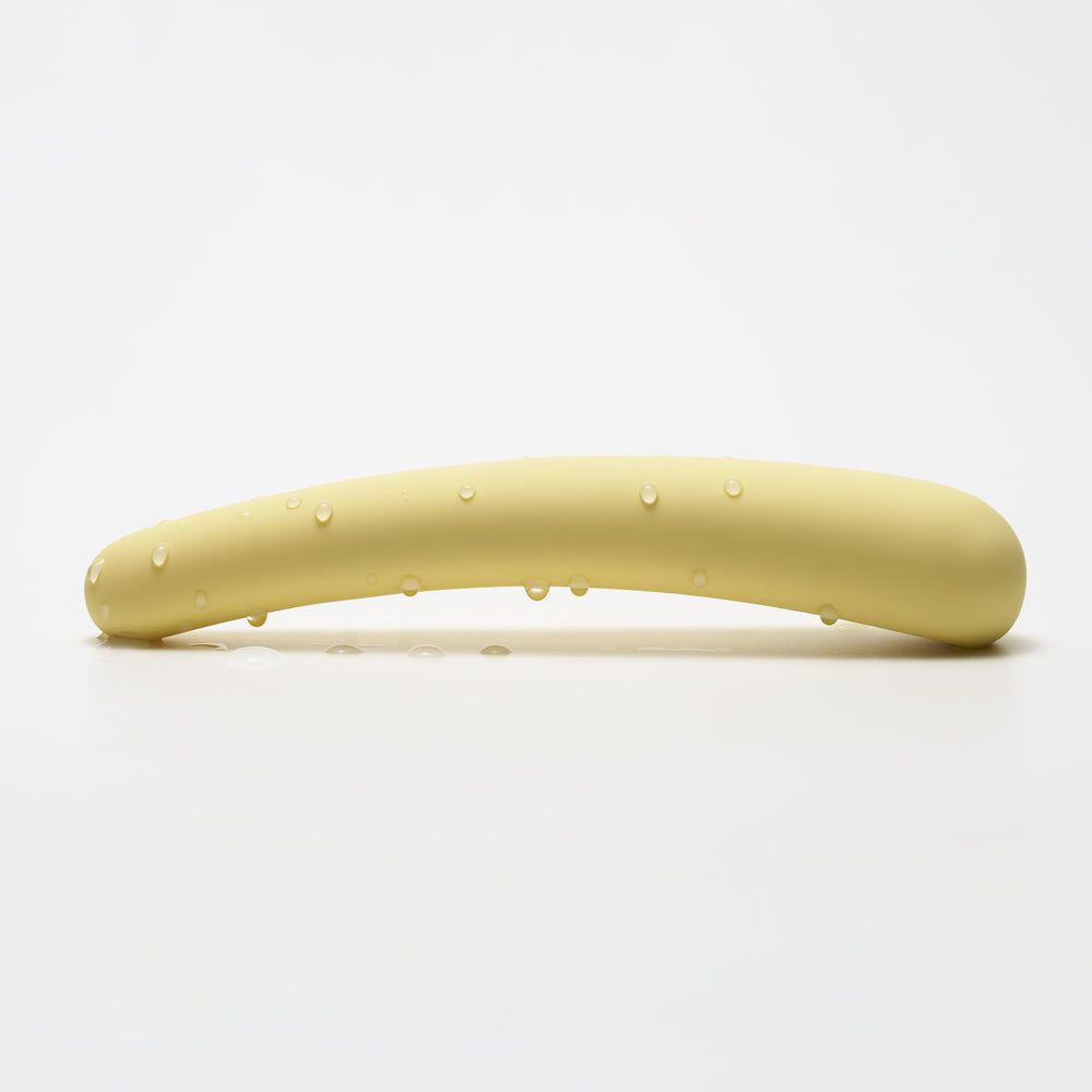 A curved, pale yellow silicone vibrator with water droplets.
