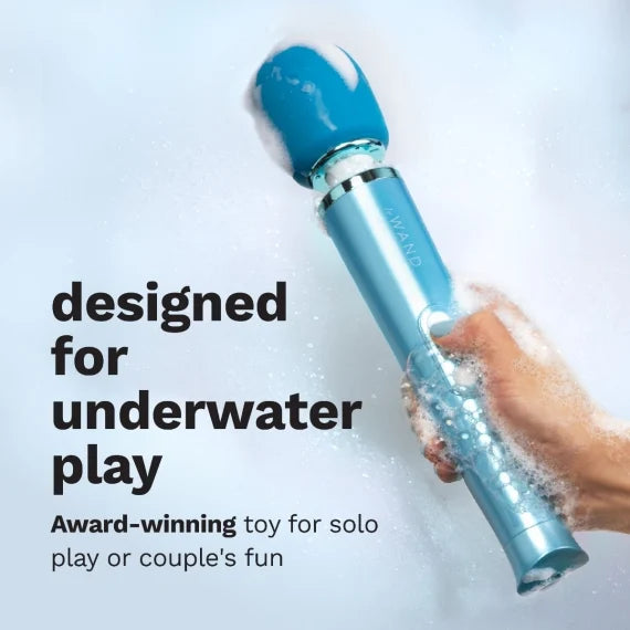 A blue waterproof wand massager with a hand holding it in bubbly water.