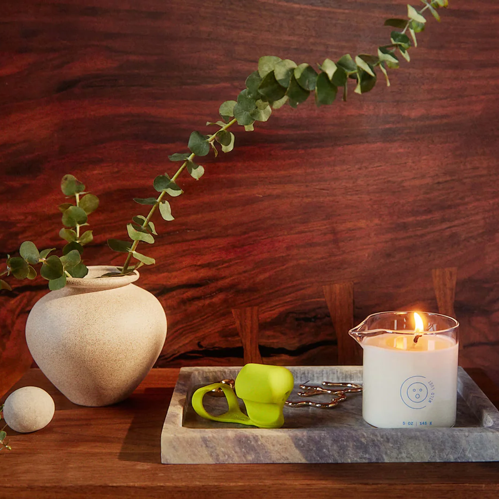 A lit massage oil candle with a pour spout on a marble tray.