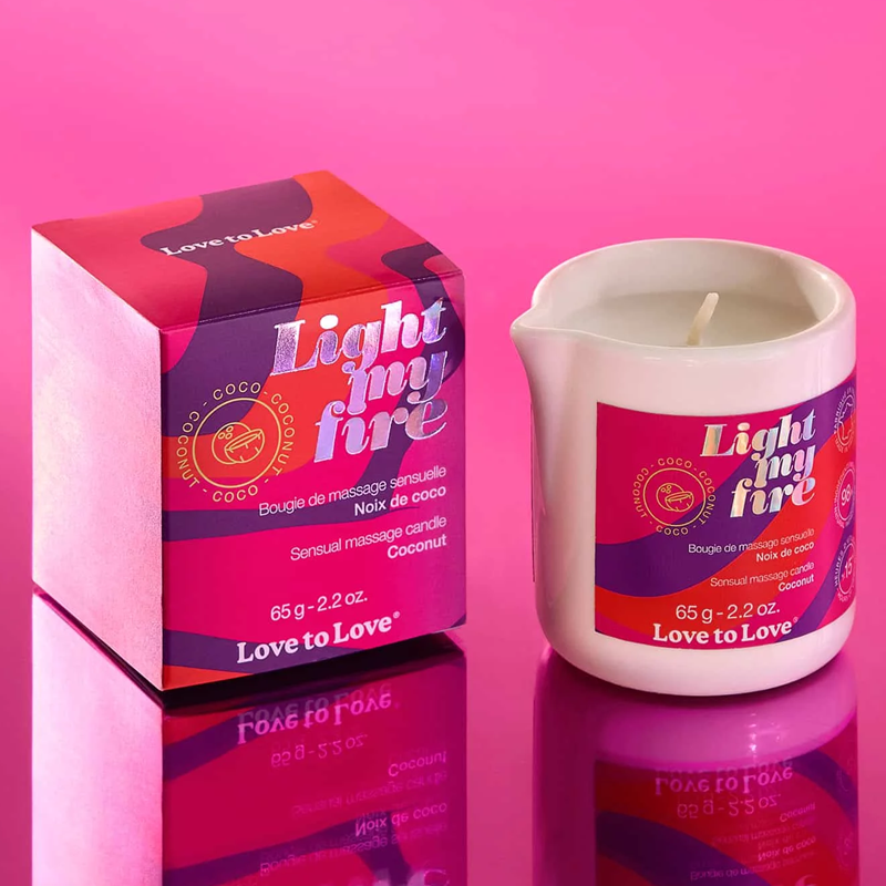 A coconut scented massage candle in a white ceramic pitcher next to its box.