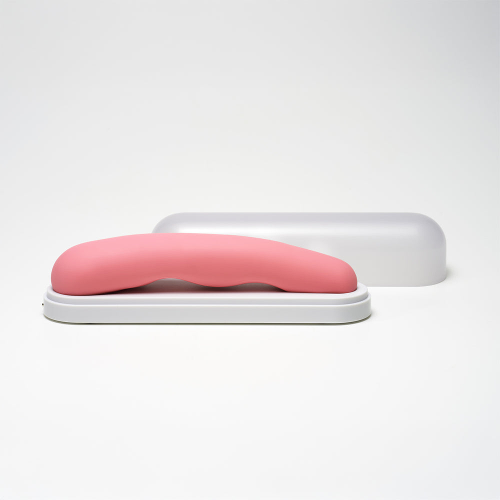 Pink G-spot vibrator with a curved design on a white base, with a translucent cover behind it.