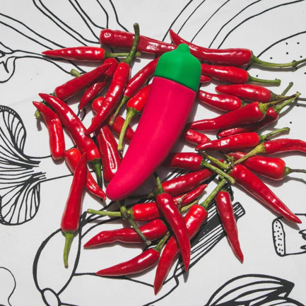 A red chili pepper shaped vibrator with a green tip surrounded by real chili peppers.