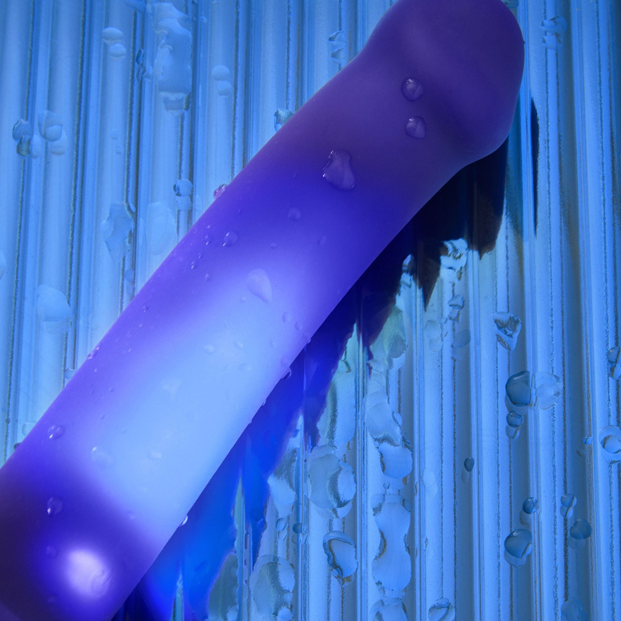 Purple silicone dildo with water droplets and blue ribbed background.