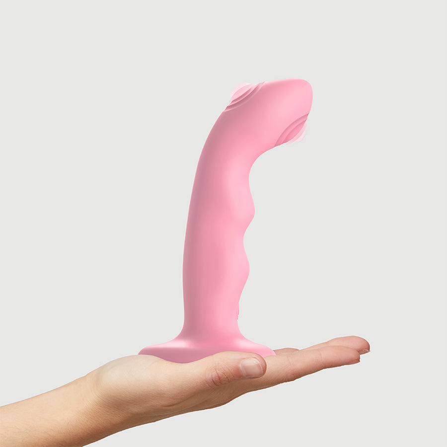 Pink silicone tapping dildo with curved wavy shape and handle, held in hand.