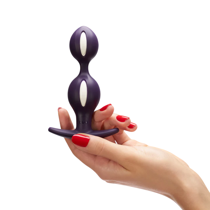A purple weighted anal plug with white accents held by a hand with red nails.