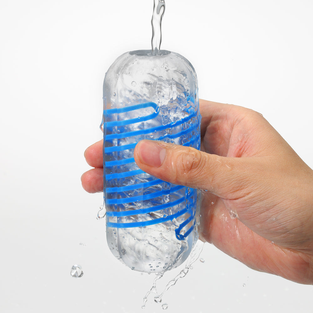A hand holds a clear stroker with blue spiral inserts as water flows over it.