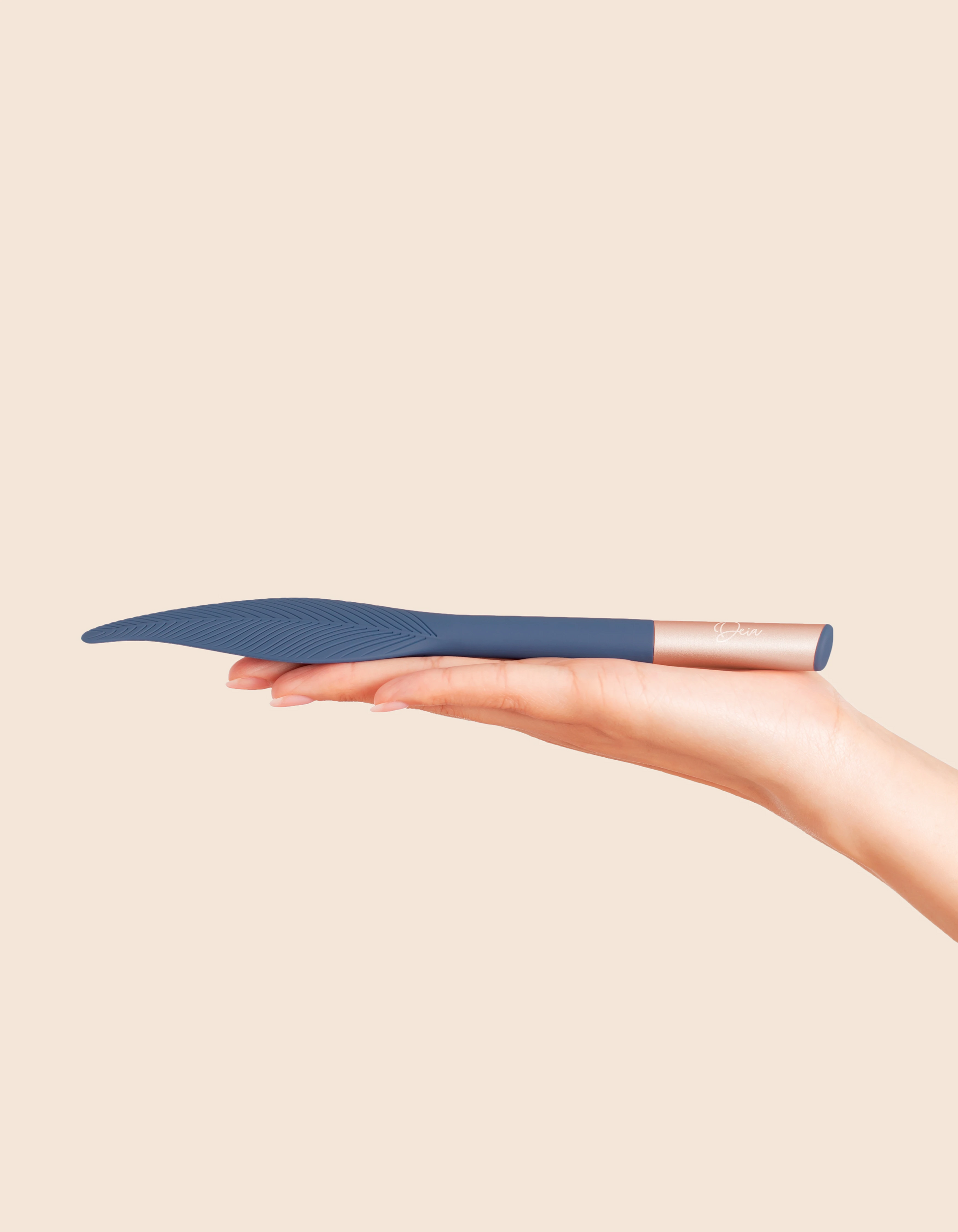 A hand holds a blue feather-shaped vibrator with a rose gold handle.