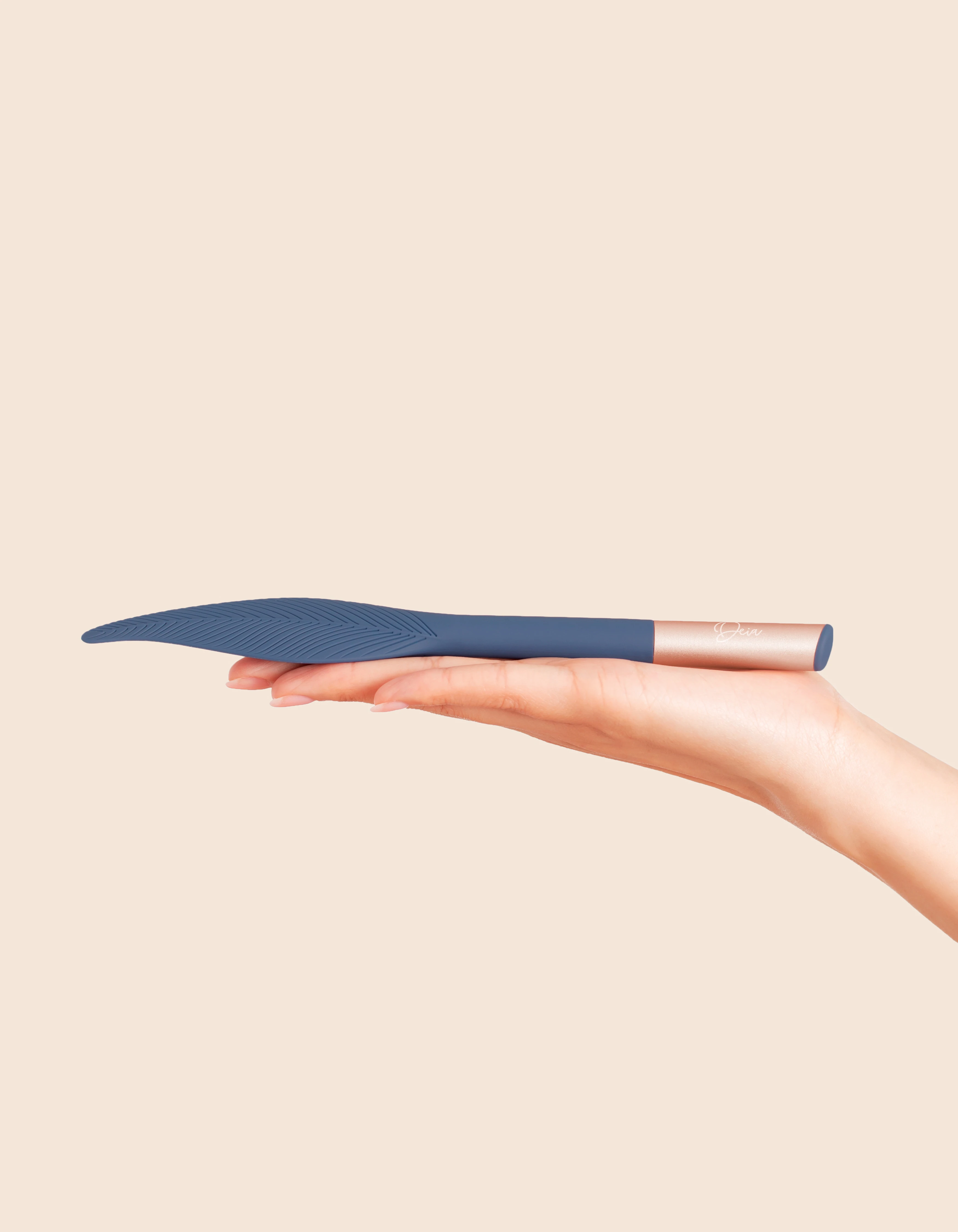 A hand holds a blue feather-shaped vibrator with a rose gold handle.