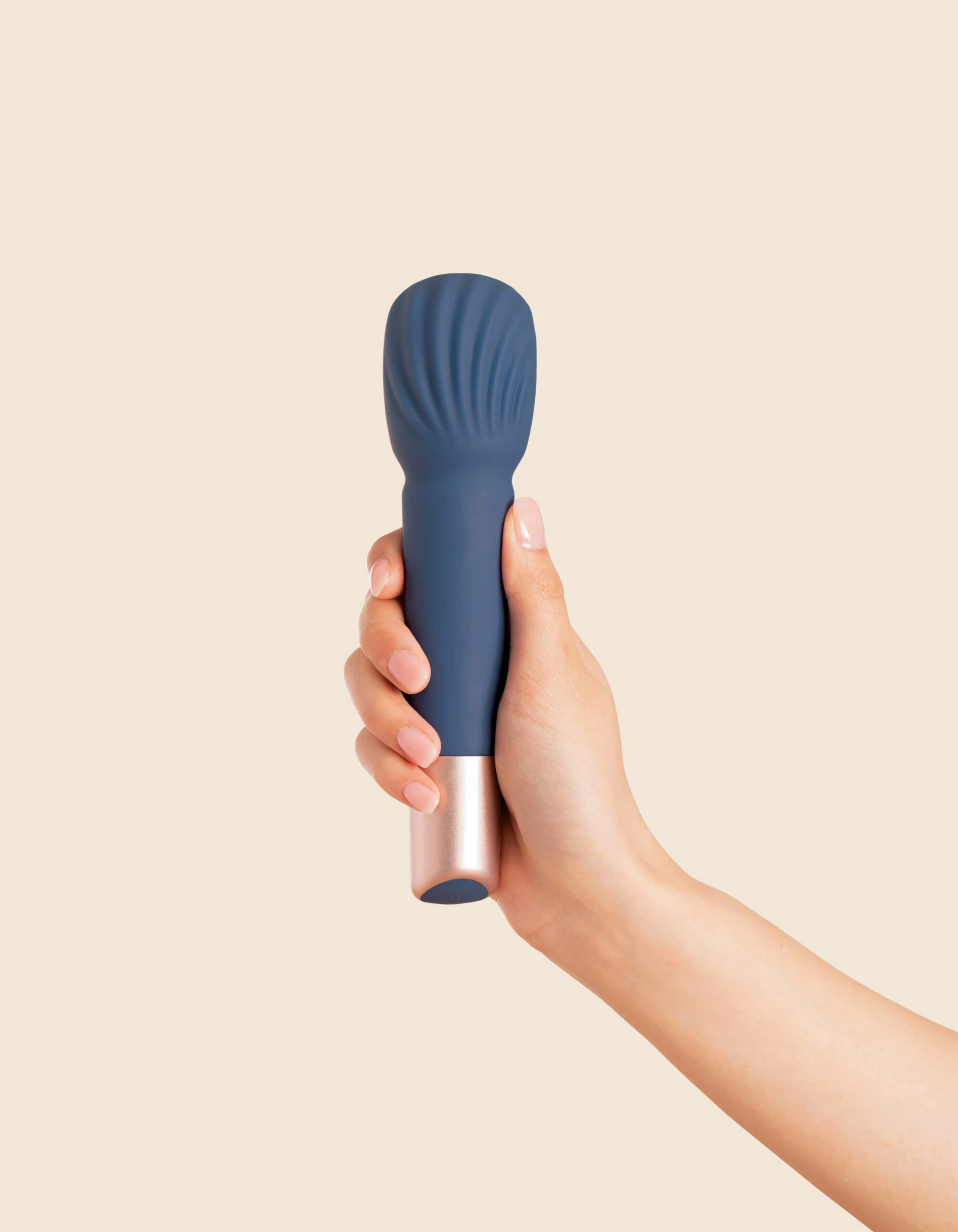 A hand holds a blue silicone massage wand with a rose gold base.